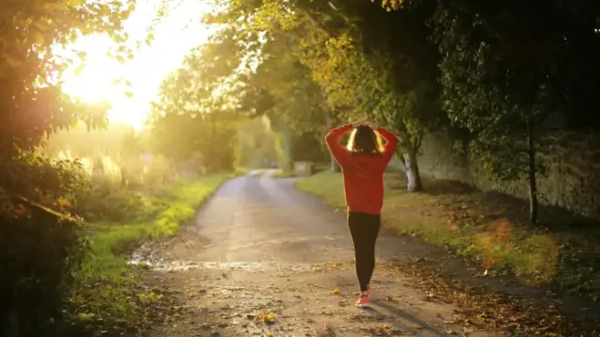 Eine Frau läuft energiegeladen eine sonnenbeschienene Straße entlang und verkörpert Vitalität und Gesundheit