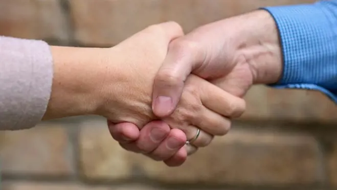 A man and woman shaking hands in front of a textured brick wall, symbolizing agreement or partnership