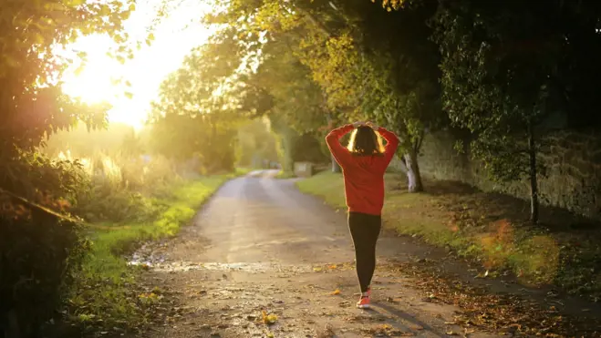 A woman runs energetically down a sunlit road, embodying vitality and health