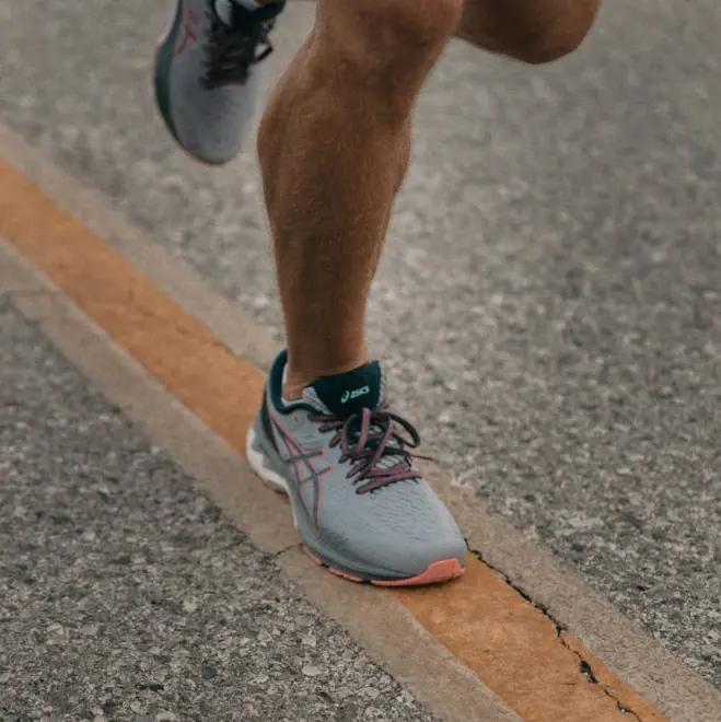 Runner in gray sneakers jogging on a road, focusing on their legs. The scene conveys motion and determination, with a visible yellow line.