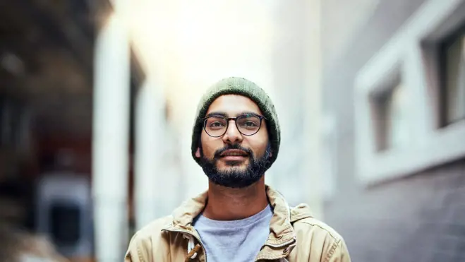 Young man with glasses and a beard poses on an urban street, noted for his role as a sperm donor