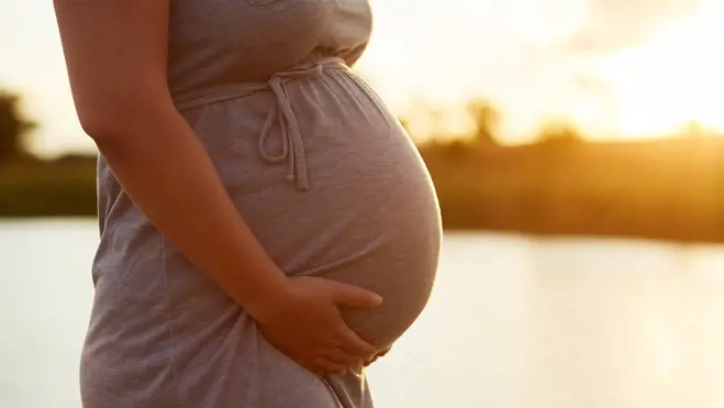 Pregnant woman holding her belly outdoors at sunset