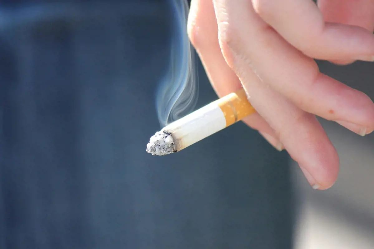 Hand holding a lit cigarette showing how smoking negatively affects sperm survival and male fertility