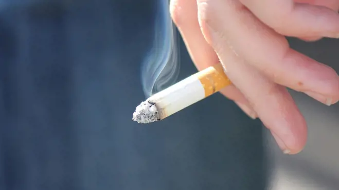 Hand holding a lit cigarette showing how smoking negatively affects sperm survival and male fertility