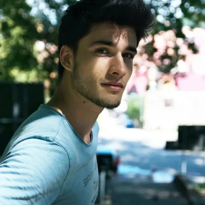 A man wearing a blue shirt stands on a city street, surrounded by buildings and pedestrians.